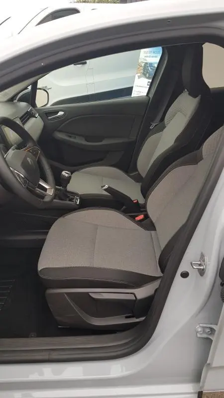Vue intérieure côté conducteur de la Renault Clio gris 2025, montrant les sièges tissu et la boîte manuelle.