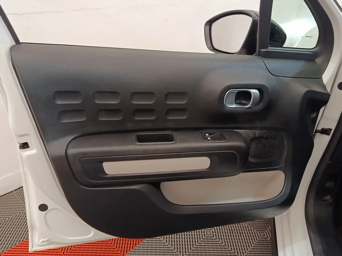 Vue rapprochée de la porte avant gauche blanche d'une Citroën C3 avec panneau intérieur noir et beige.