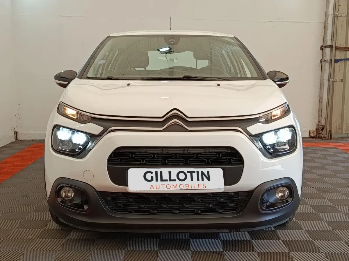 Vue avant d'une Citroën C3 blanche de 2022 avec phares LED allumés dans un garage.