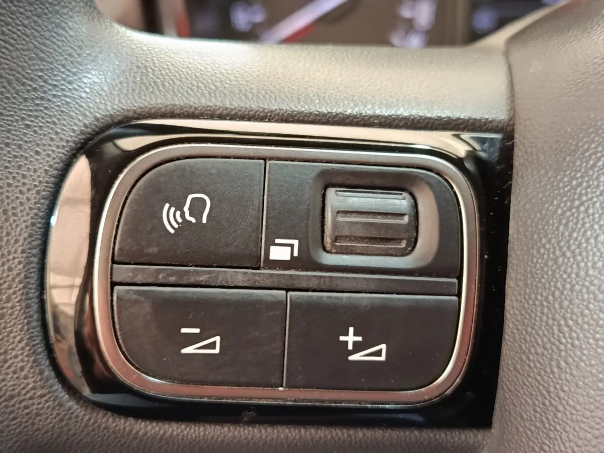 Gros plan sur les commandes de volume et reconnaissance vocale sur le volant noir de la Citroën C3 blanche.
