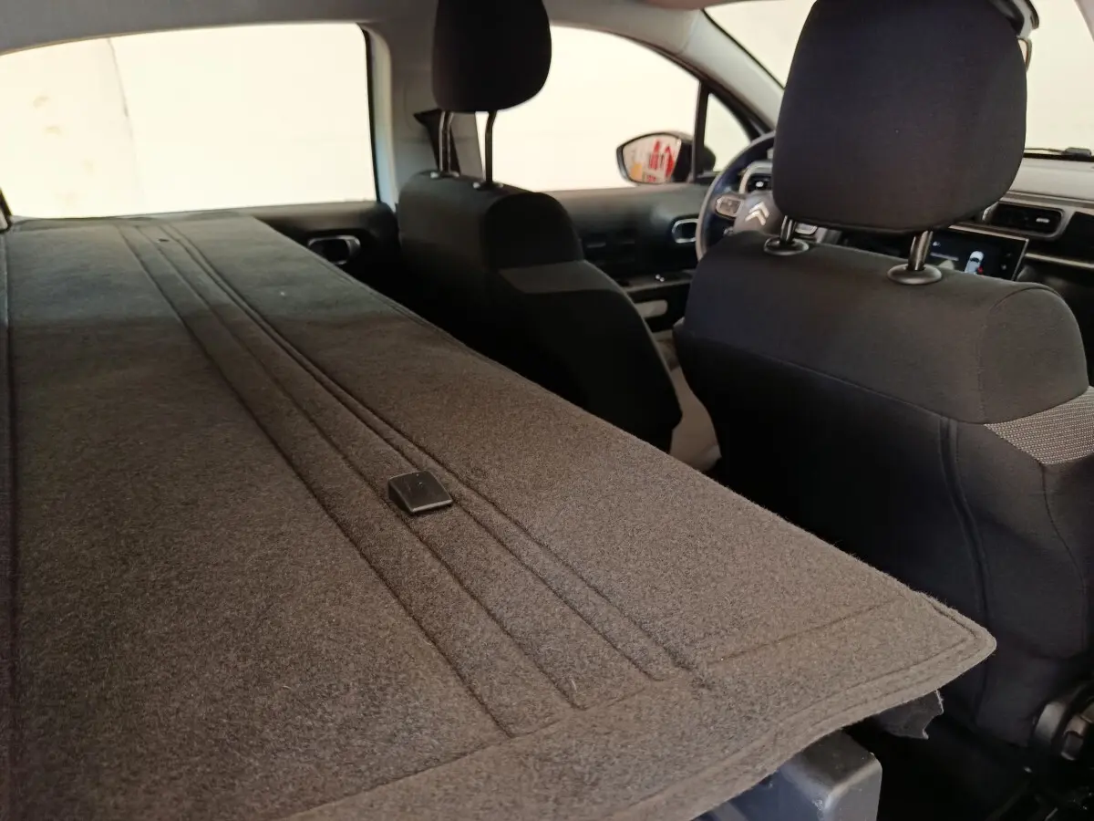 Vue intérieure arrière de la Citroën C3 blanche 2022 avec banquette rabattue et sièges avant noirs.