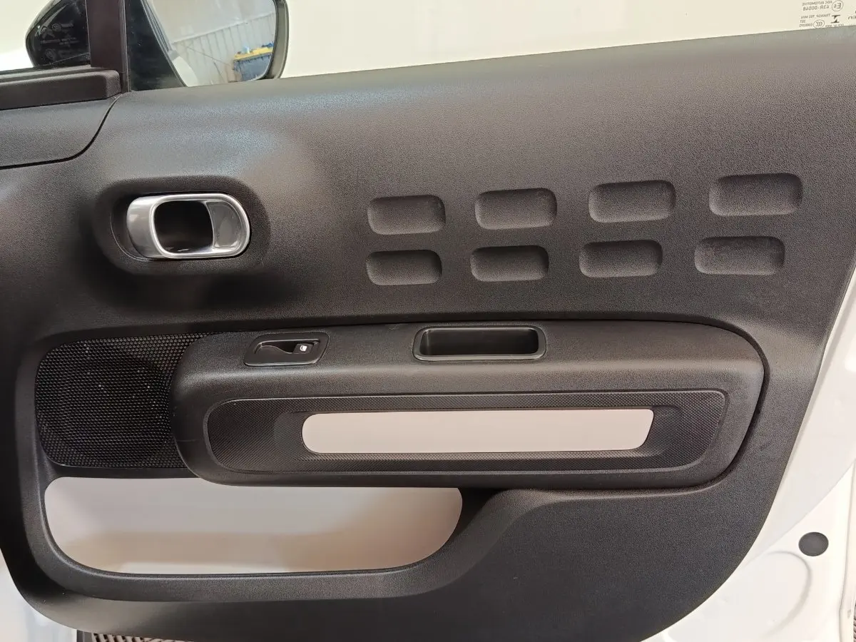 Gros plan sur la porte intérieure côté gauche de la Citroën C3 blanche, avec poignée chromée et inserts noirs texturés.