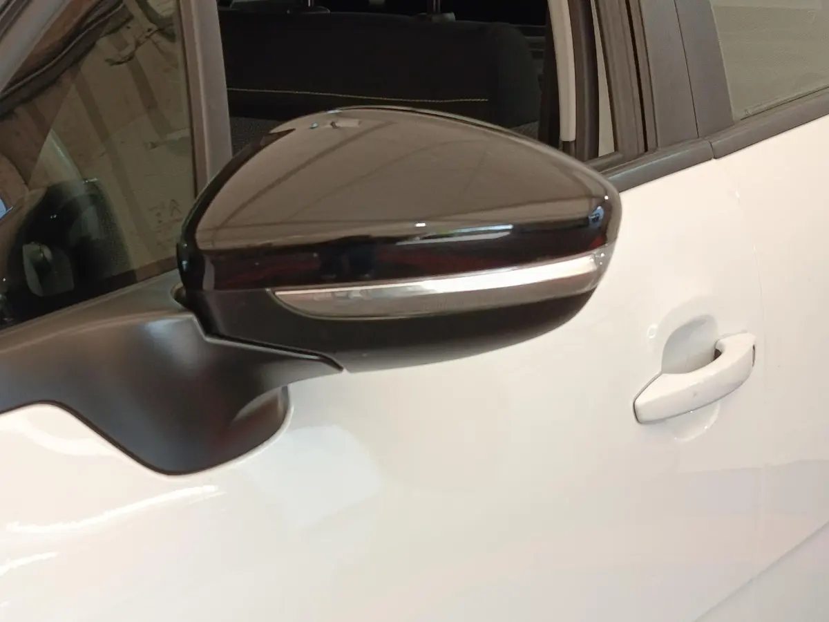 Gros plan sur le rétroviseur noir brillant côté gauche d'une Citroën C3 blanche avec poignée de porte visible.