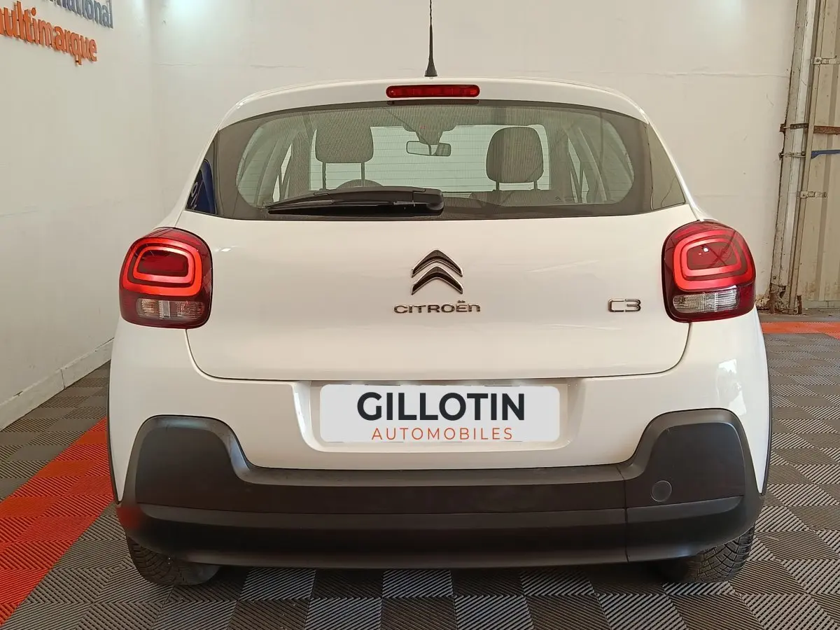 Vue arrière d'une Citroën C3 blanche 2022 avec feux arrière LED et pare-chocs noir mat en intérieur showroom.