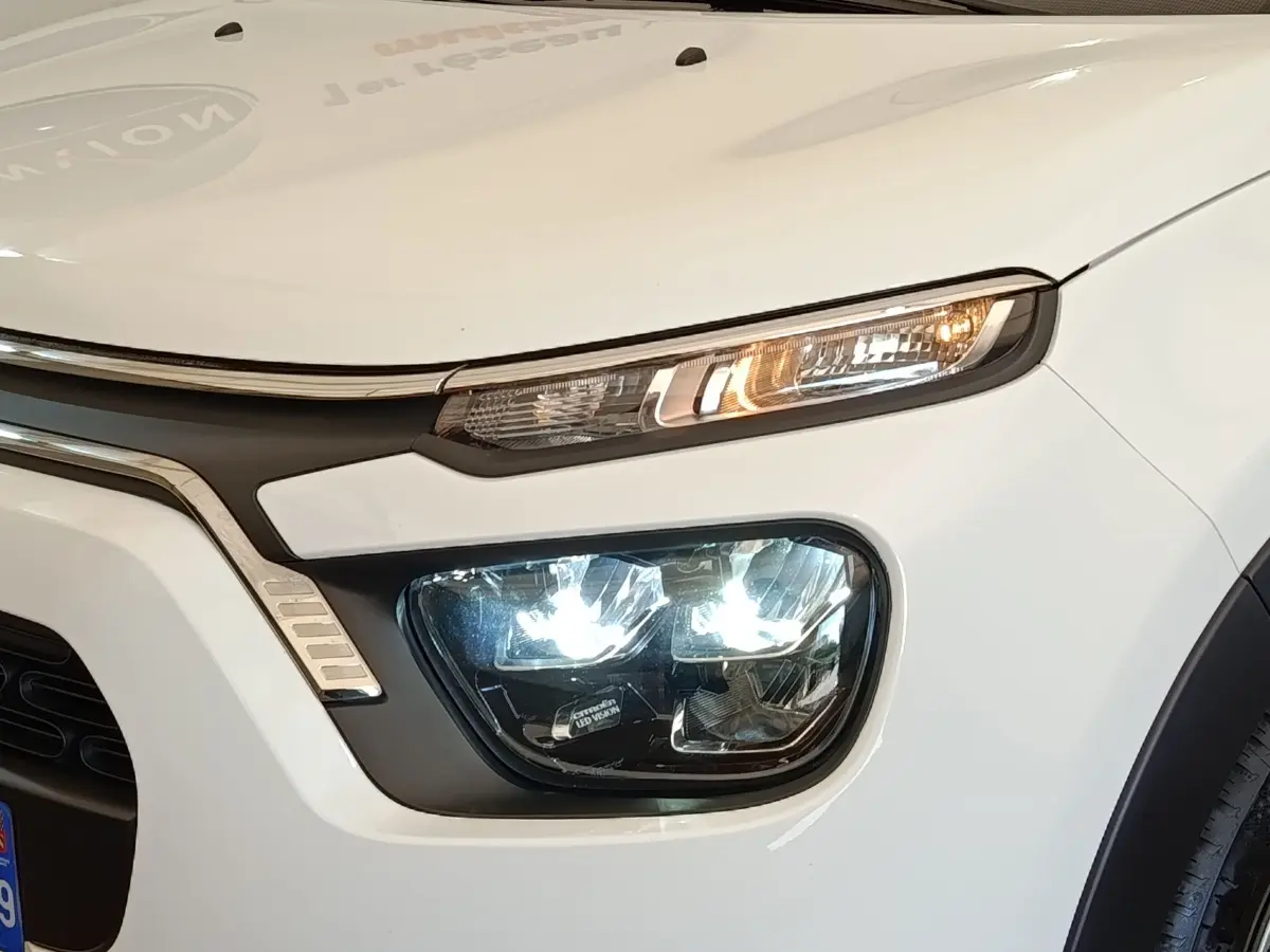 Gros plan sur l'avant droit blanc d'une Citroën C3 2022 avec phares LED allumés et calandre noire.