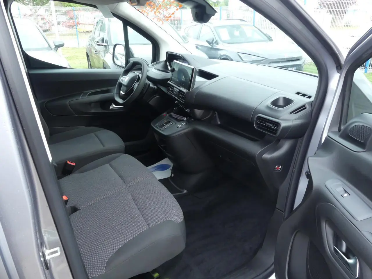 Intérieur avant droit du Peugeot Partner gris métallisé 2025, montrant sièges tissu et tableau de bord moderne.
