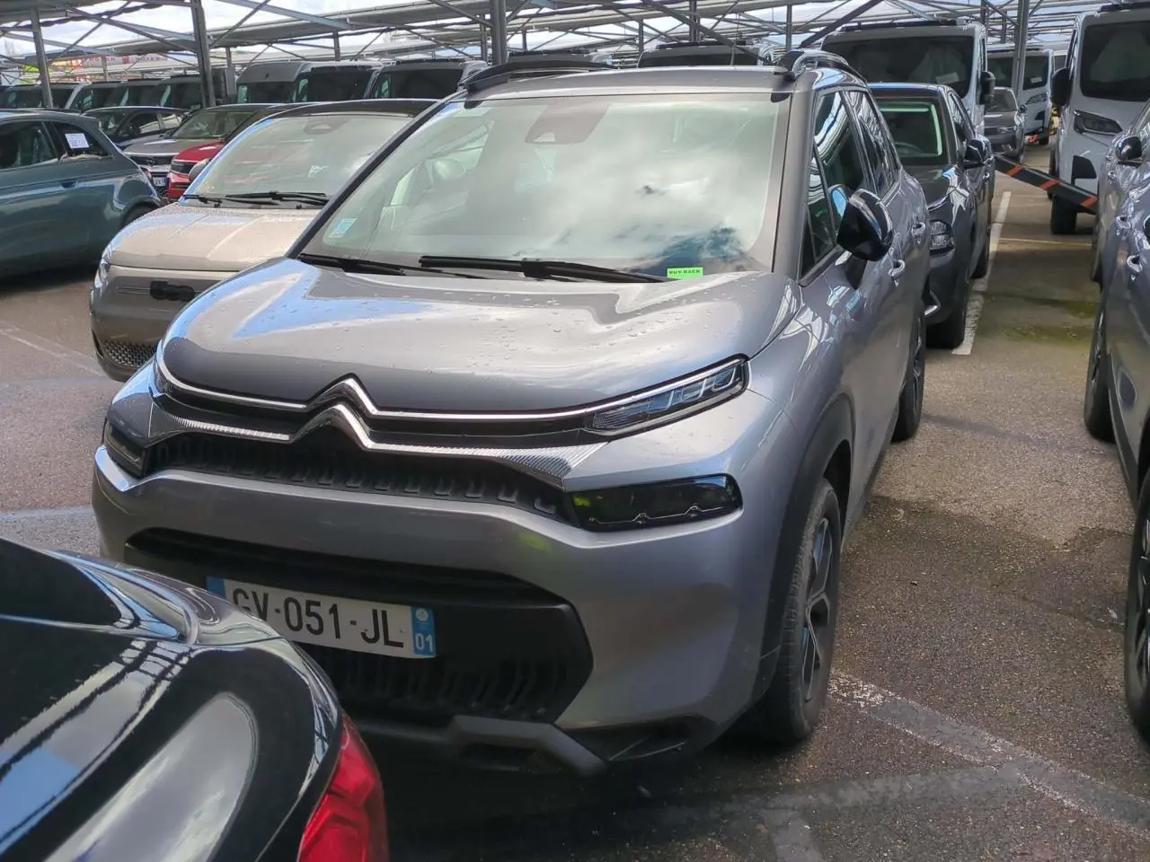 Citroën C3 Aircross gris foncé vue 3/4 avant droit avec barres de toit noir brillant en parking couvert.