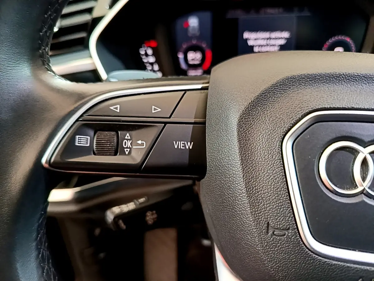 Gros plan sur le volant cuir noir d'un Audi Q3 2021 avec commandes multifonctions et logo Audi visible au centre.