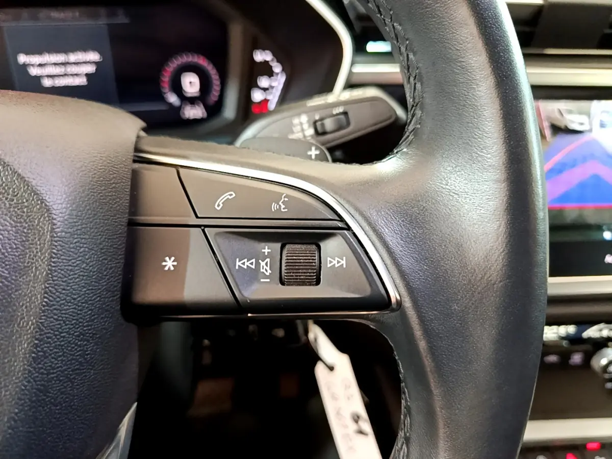 Gros plan sur les commandes gauche du volant cuir noir de l'Audi Q3 35 TDI 2021 avec affichage numérique en arrière-plan.