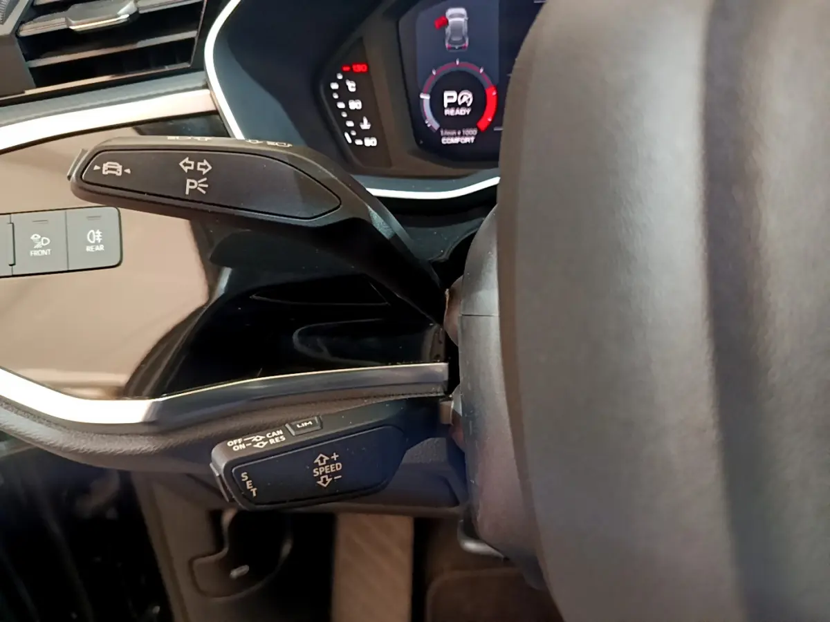 Gros plan sur les commandes au volant d'un Audi Q3 noir 2021, affichage digital et leviers multifonctions visibles.