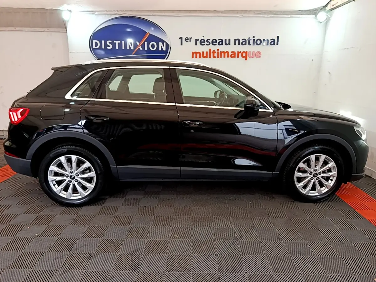 Profil côté gauche d'un Audi Q3 noir 2021 garé en intérieur avec jantes alliage et feux arrière LED allumés.