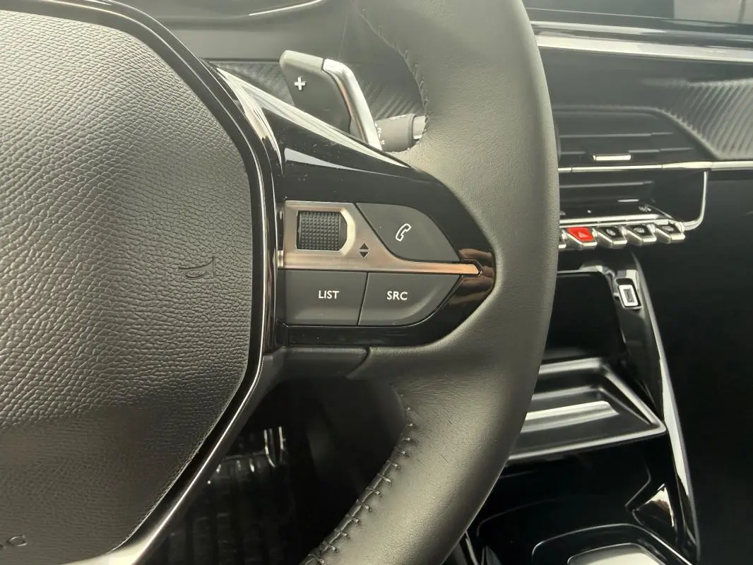Gros plan sur le volant noir et les commandes multimédia du Peugeot 208 Hybrid 145 Allure, intérieur moderne et épuré.