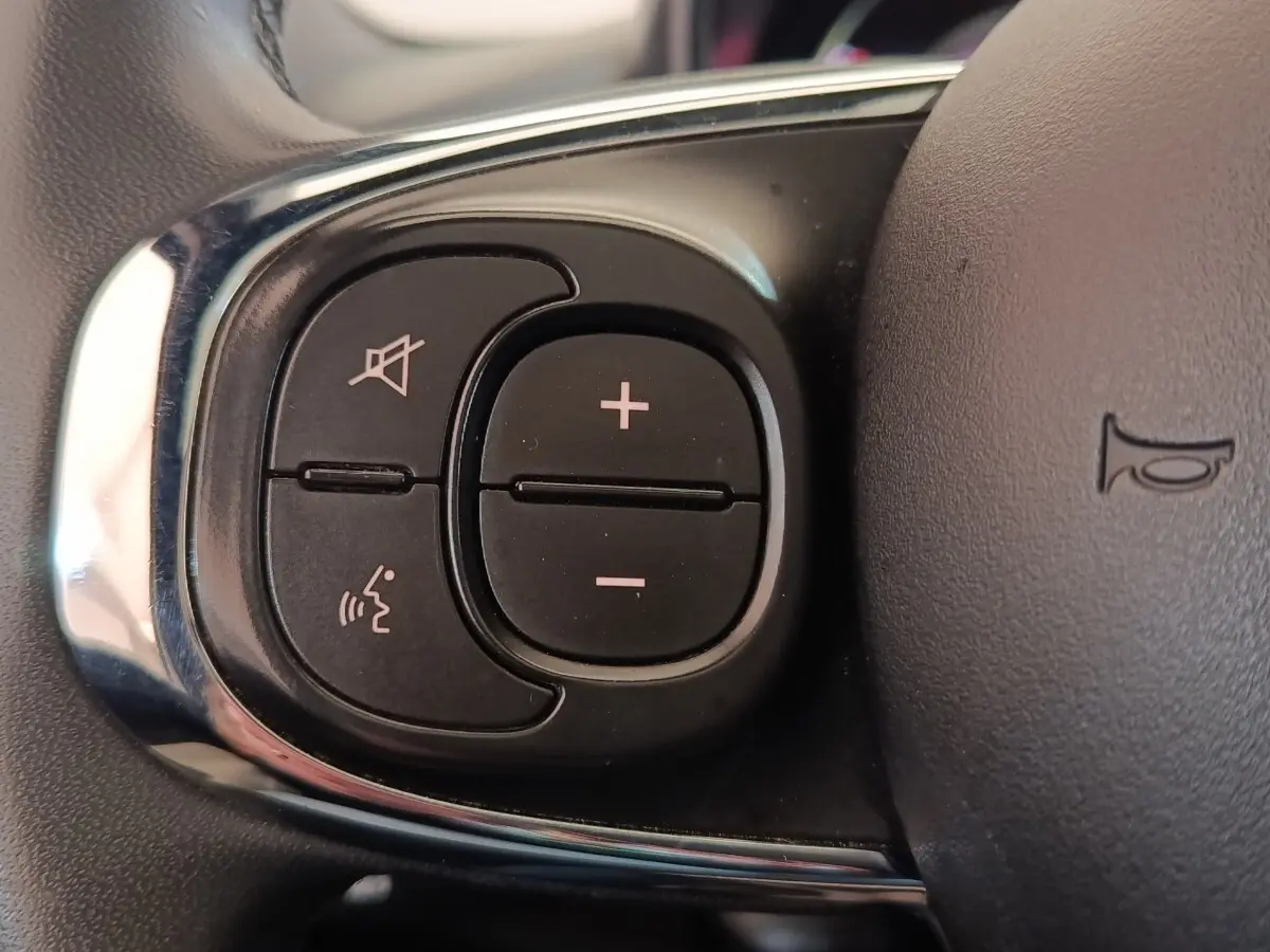 Gros plan sur les commandes du volant cuir noir de la Fiat 500 Hybrid Dolcevita 2022, boutons de volume et reconnaissance vocale.