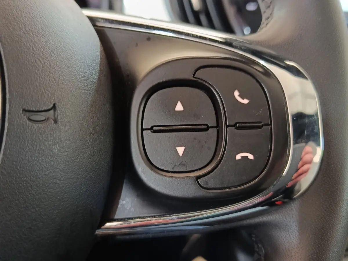 Gros plan sur les commandes du volant cuir de la FIAT 500 Hybrid blanc, boutons de gestion d’appel et navigation.