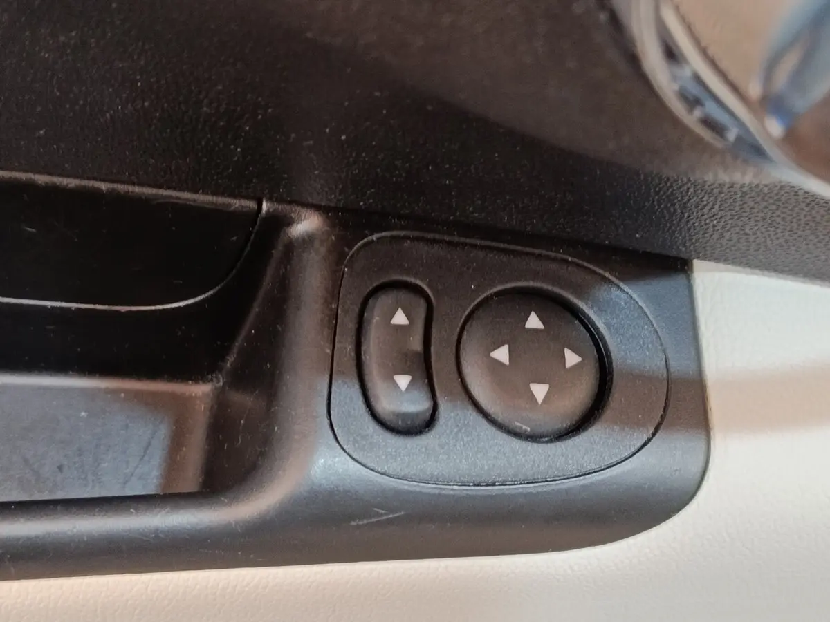 Gros plan sur les commandes de réglage des rétroviseurs intérieures noires sur panneau beige d'une Fiat 500 blanche.