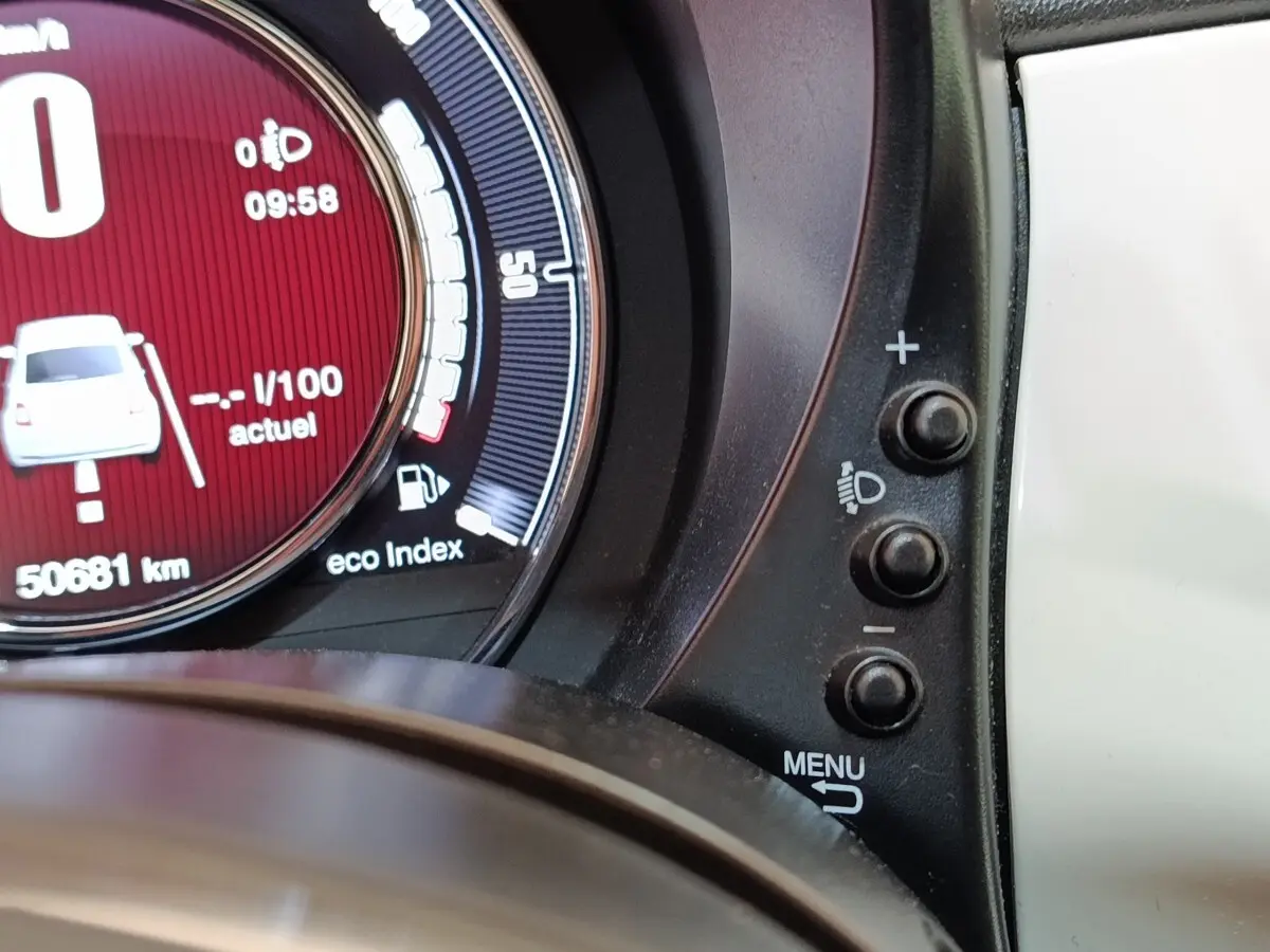 Gros plan sur le compteur digital rouge de la Fiat 500 blanche, avec boutons de réglage des phares à droite.