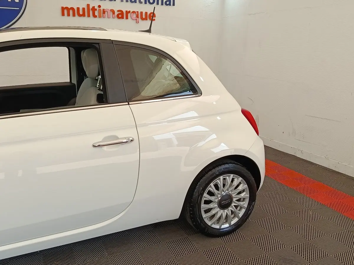 Profil arrière droit de la FIAT 500 blanche, mettant en valeur la roue et la porte arrière dans un intérieur showroom.