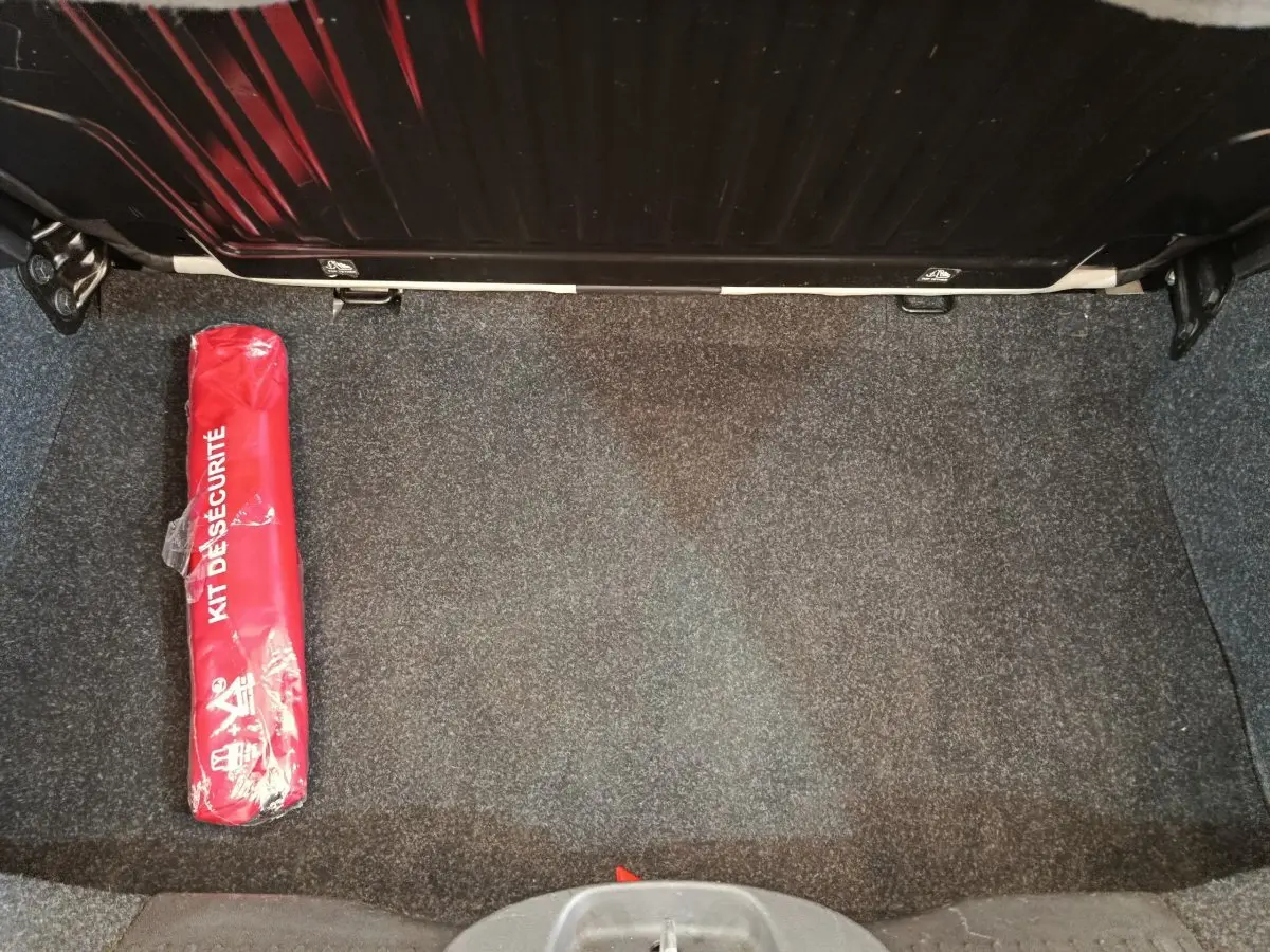 Coffre ouvert d'une Fiat 500 blanche, vue de dessus, avec un kit de sécurité rouge posé à gauche.