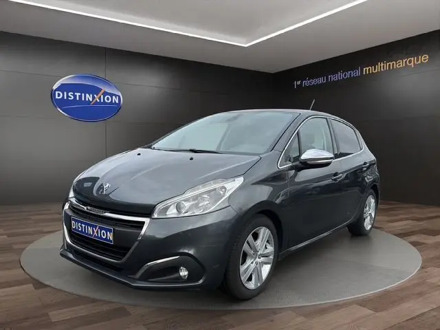 Peugeot 208 gris platinium vue 3/4 avant droit, avec rétroviseurs chromés et feux LED dans un showroom.