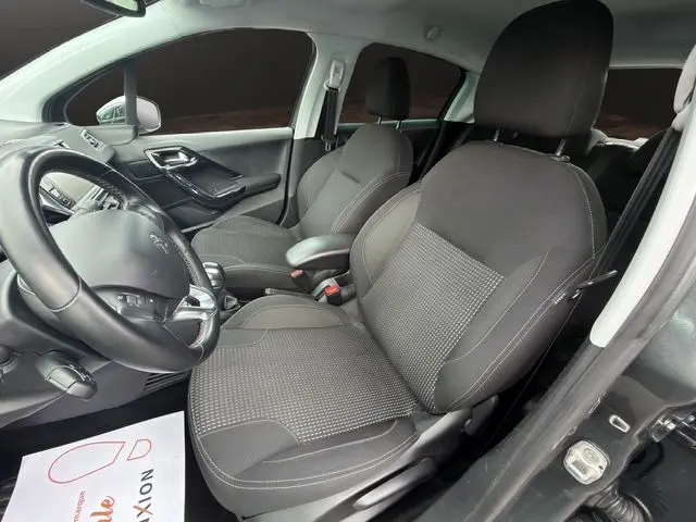 Vue intérieure côté gauche de la Peugeot 208 gris platinium, sièges tissu noirs et volant cuir multifonctions.
