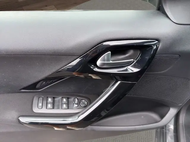 Gros plan sur la poignée intérieure et les commandes de porte côté conducteur de la Peugeot 208 gris platinium.