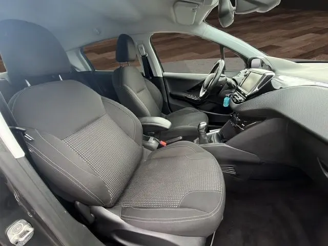 Vue intérieure côté gauche de la Peugeot 208 gris platinium, montrant sièges tissu, volant cuir multifonctions et tableau de bord tactile.