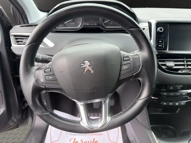 Vue rapprochée du volant cuir noir multifonctions de la Peugeot 208 gris platinium, avec tableau de bord et écran tactile visibles.