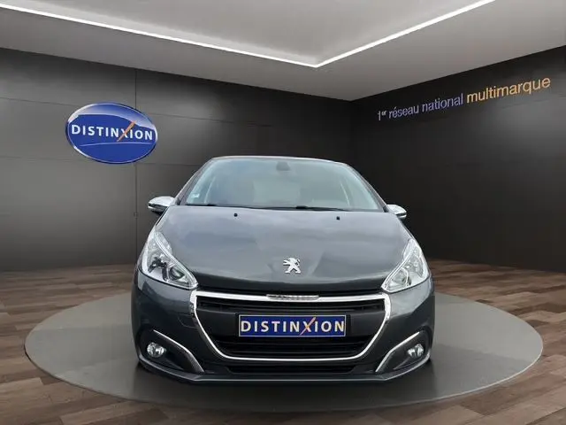 Vue avant d'une Peugeot 208 gris platinium exposée en showroom avec logo Distinxion sur fond noir.