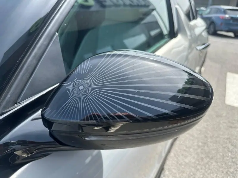 Gros plan sur le rétroviseur côté gauche noir brillant avec motif rayonnant, sur DS3 1.2 PureTech 130ch Cristal Pearl 2024.