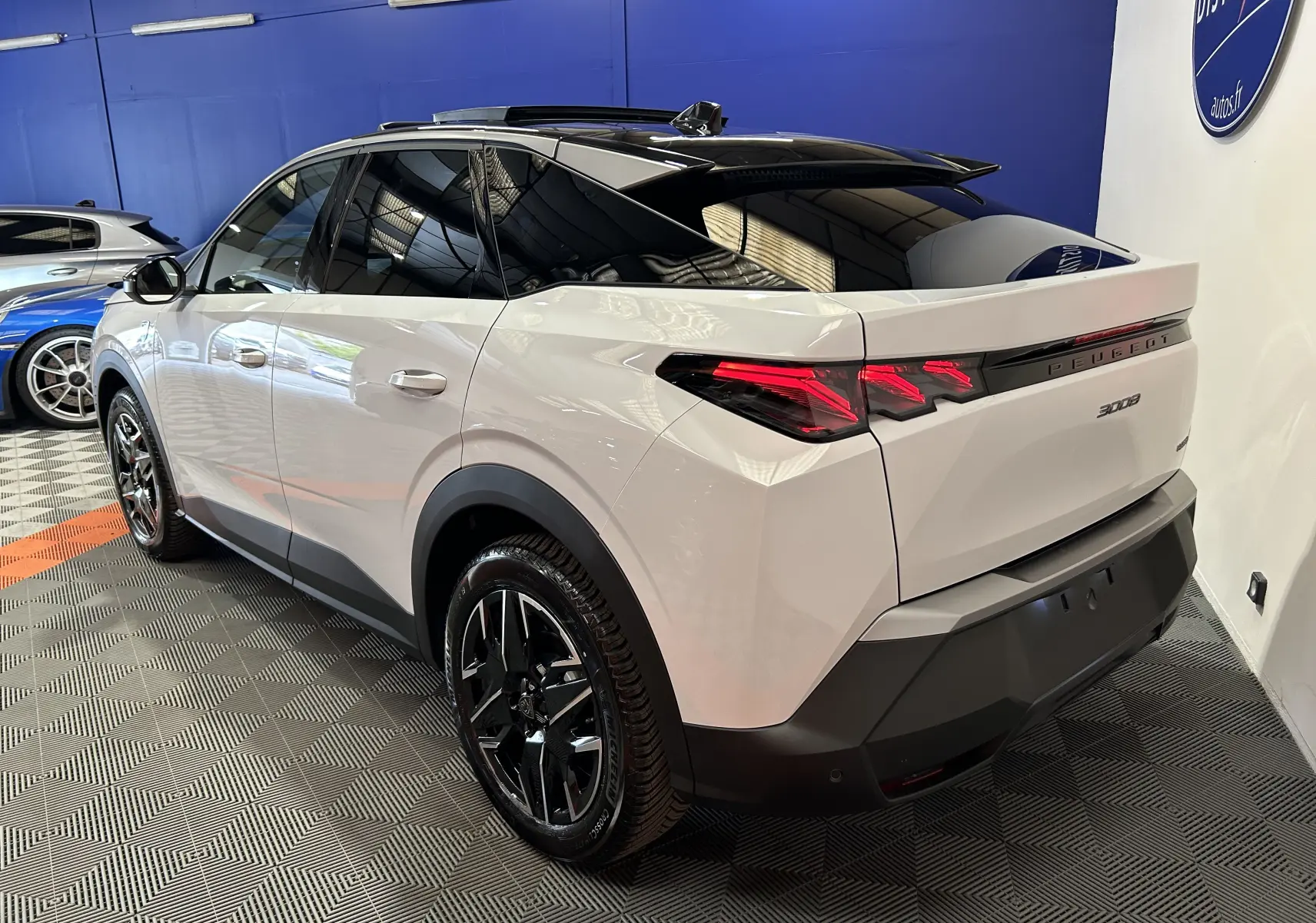 Vue 3/4 arrière droite du Peugeot 3008 Hybrid blanc Okenite avec toit panoramique et jantes noires brillantes.