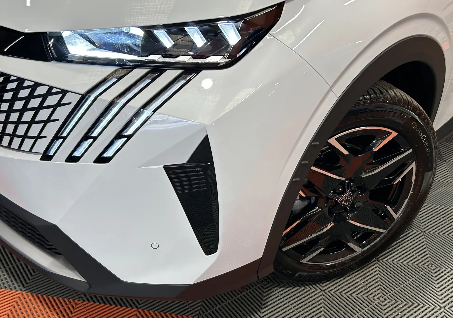 Gros plan sur l’avant droit blanc Okenite du Peugeot 3008 III Hybrid avec phares LED et jante noire biton distinctive.
