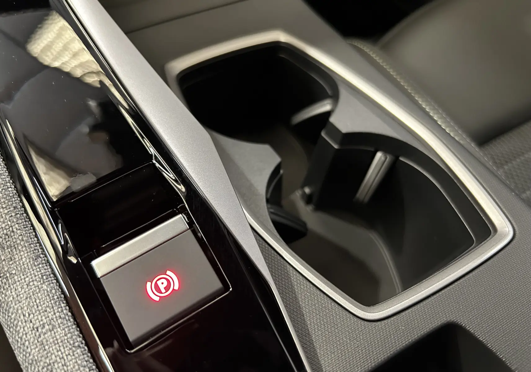 Gros plan sur la console centrale noire et grise du Peugeot 3008 Hybrid avec bouton de frein à main électronique illuminé en rouge.