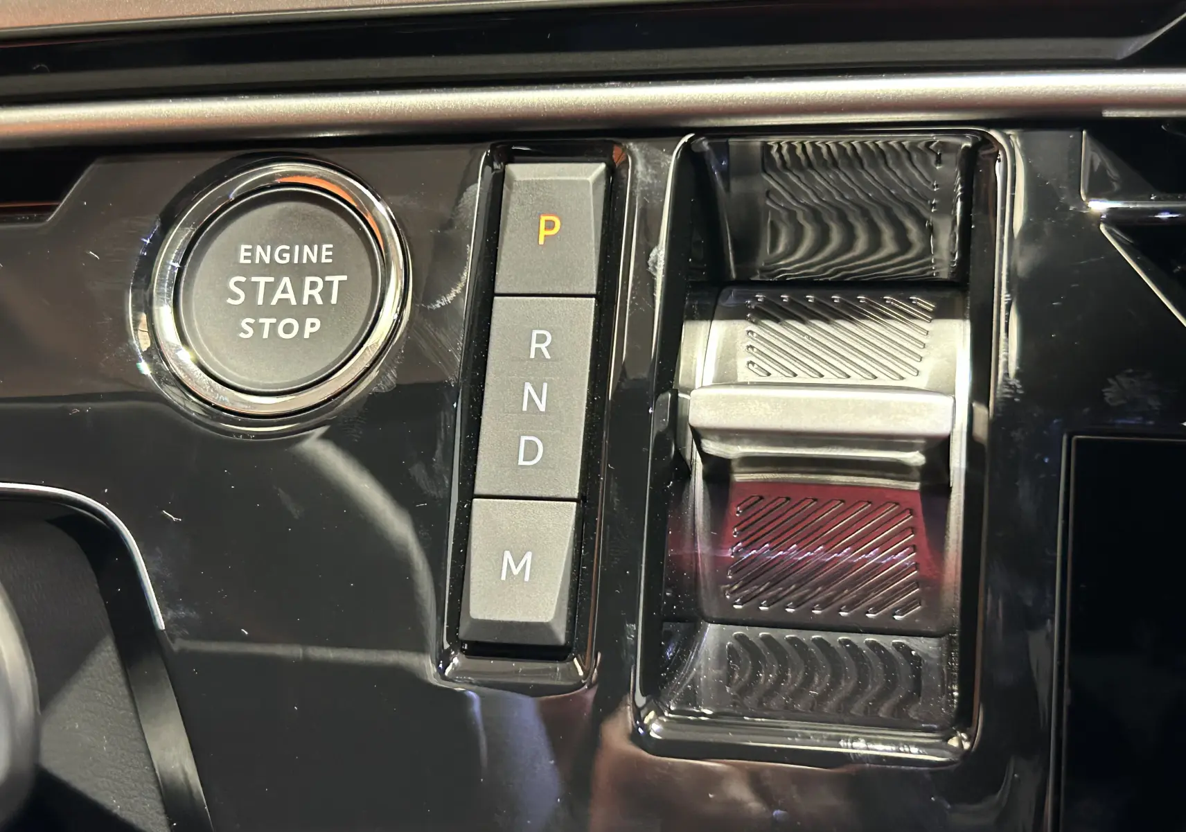 Gros plan sur la console centrale noire brillante du Peugeot 3008 Hybrid avec bouton start/stop et sélecteur de vitesses à boutons.
