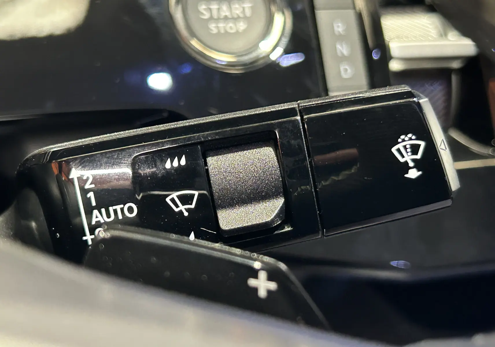 Gros plan sur la commande de l’essuie-glace noir brillant du Peugeot 3008 III Hybrid, avec bouton Start/Stop en arrière-plan.