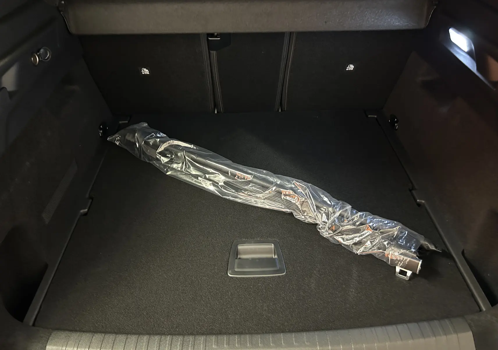 Coffre du Peugeot 3008 Hybrid blanc, vue intérieure montrant un accessoire emballé posé sur le tapis noir.