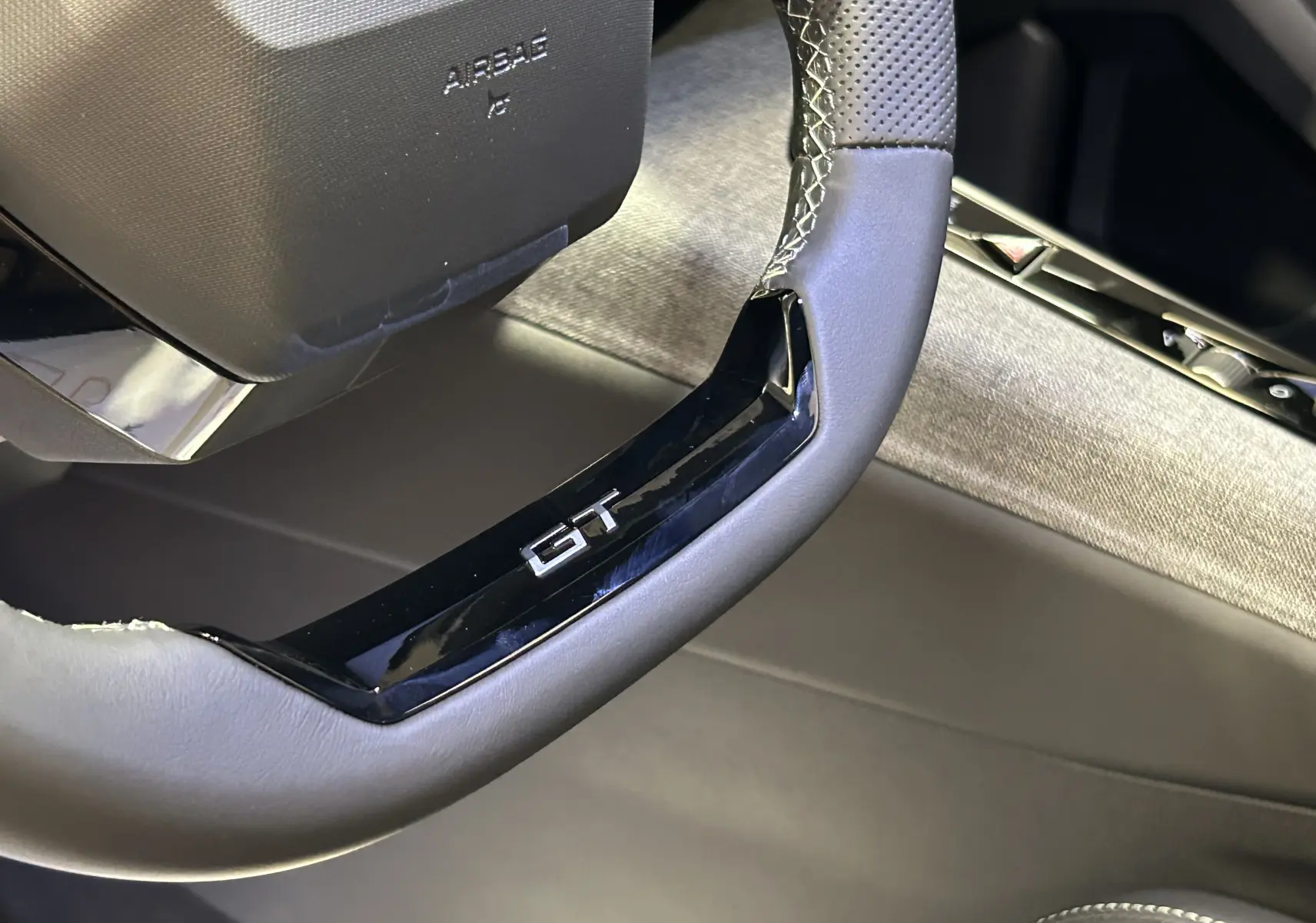 Gros plan sur le volant cuir perforé avec logo GT du Peugeot 3008 III Hybrid, intérieur gris et noir.