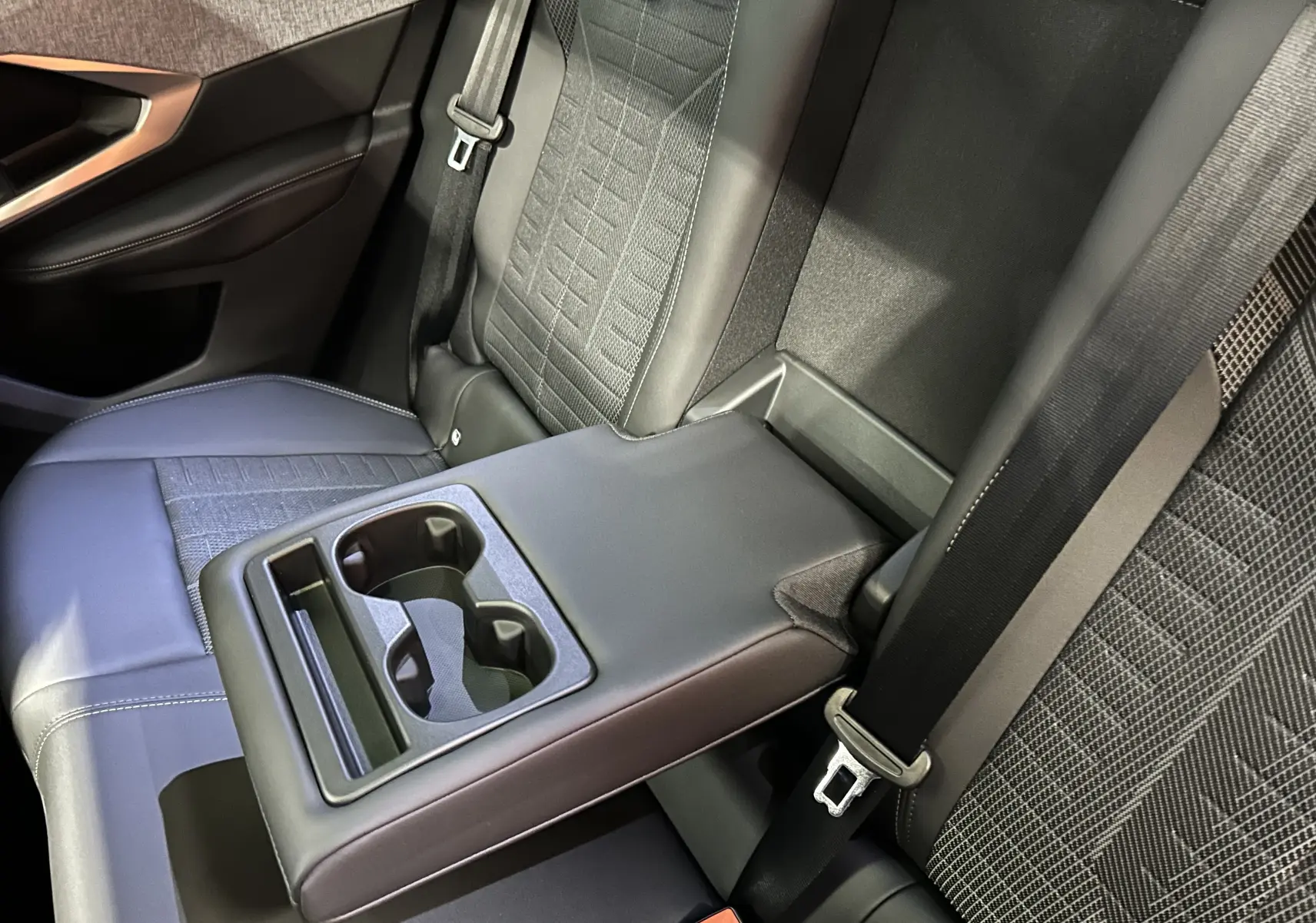 Vue rapprochée de l’accoudoir central arrière avec porte-gobelets et sièges en tissu noir du Peugeot 3008 Hybrid 2026.