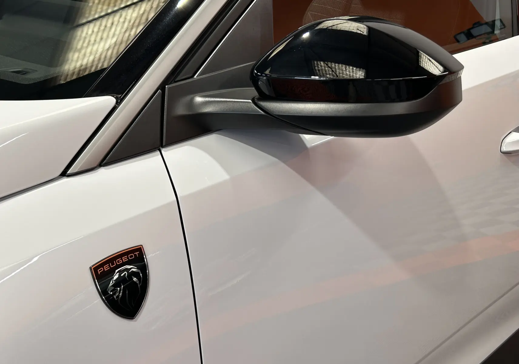 Détail du côté gauche blanc Okenite du Peugeot 3008 III Hybrid avec rétroviseur noir brillant et logo Peugeot sur l'aile.