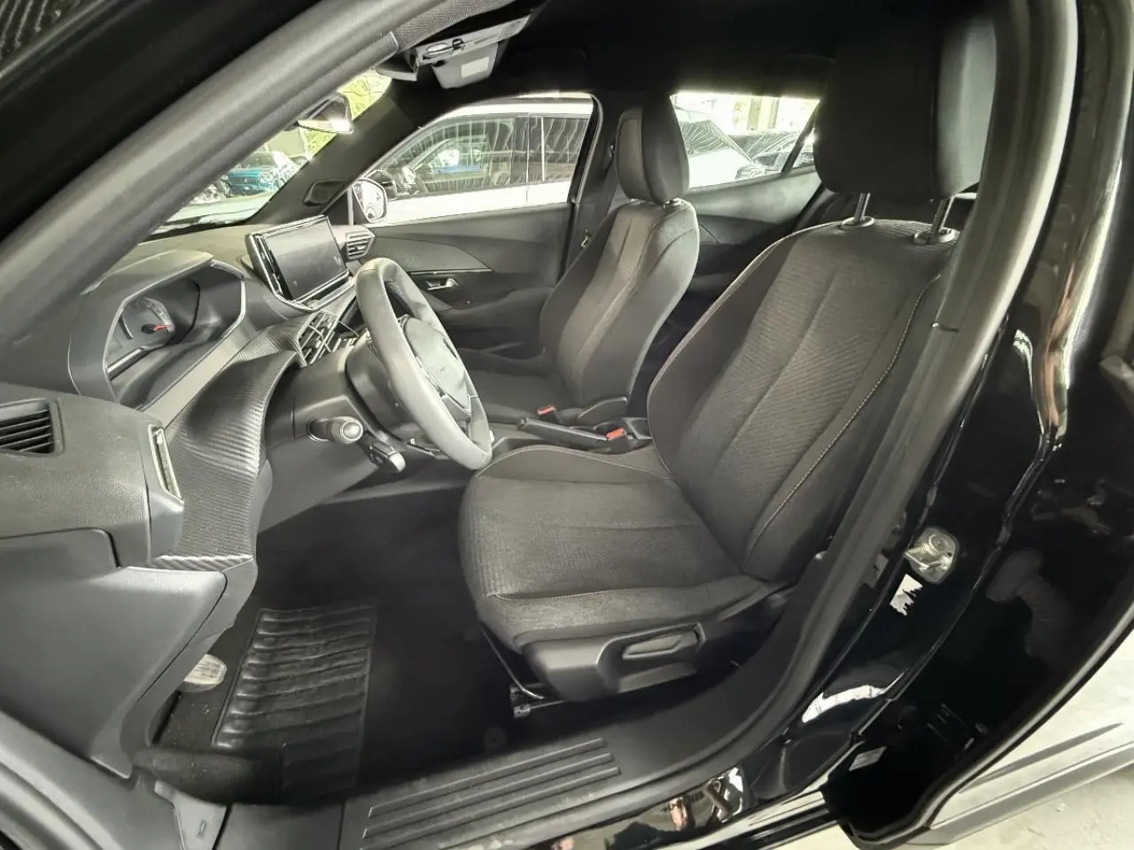 Vue intérieure côté conducteur du Peugeot 2008 noir perla 2025, montrant sièges et tableau de bord moderne.