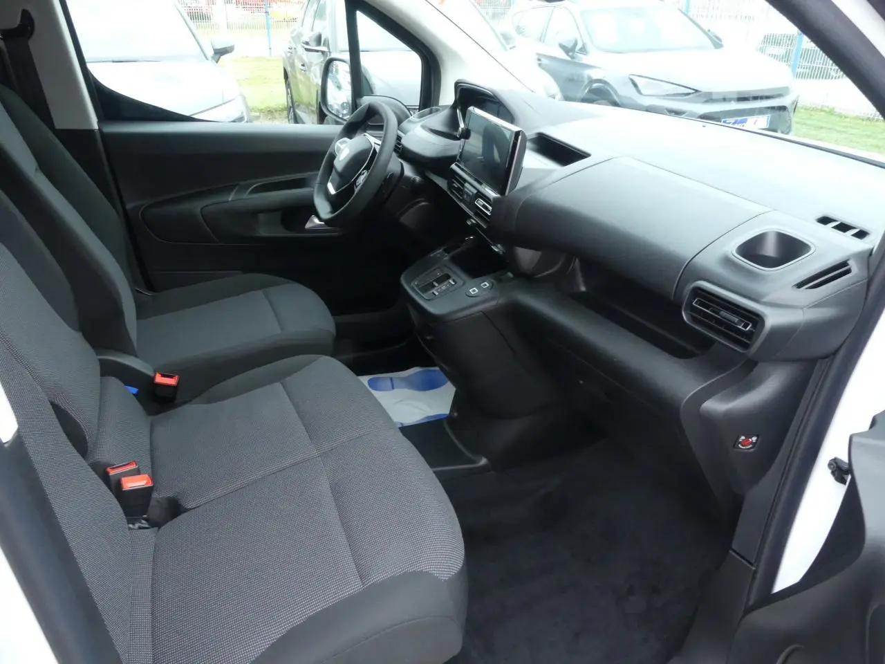 Intérieur du Peugeot Partner XL 2025 vu côté conducteur, sièges tissu gris et tableau de bord noir moderne.