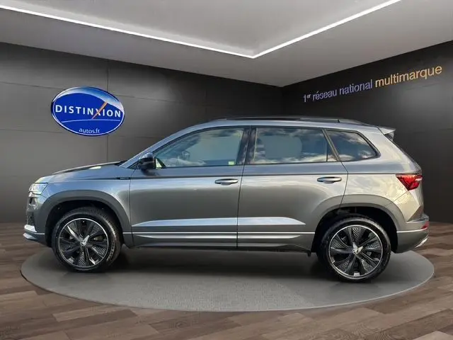 Vue de profil droit d'un Skoda Karoq gris graphite 2025 avec jantes alliage noires et attelage escamotable visible.