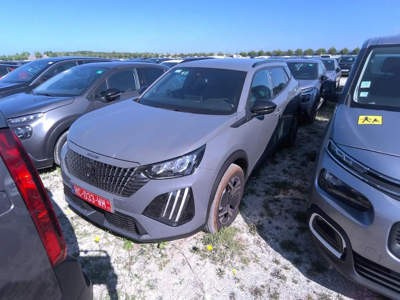 Peugeot 2008 gris clair vue 3/4 avant droit, avec calandre noire et feux LED à griffes distinctifs.