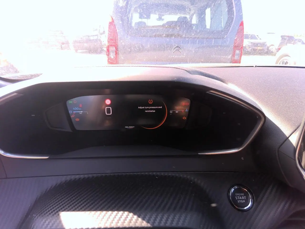 Tableau de bord intérieur noir avec écran numérique Peugeot et bouton start/stop visible en gros plan.