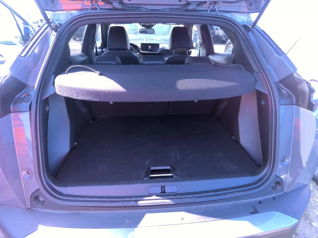Coffre ouvert vu de l'arrière d'un Peugeot 2008 gris clair, avec cache-bagages et intérieur noir visible.