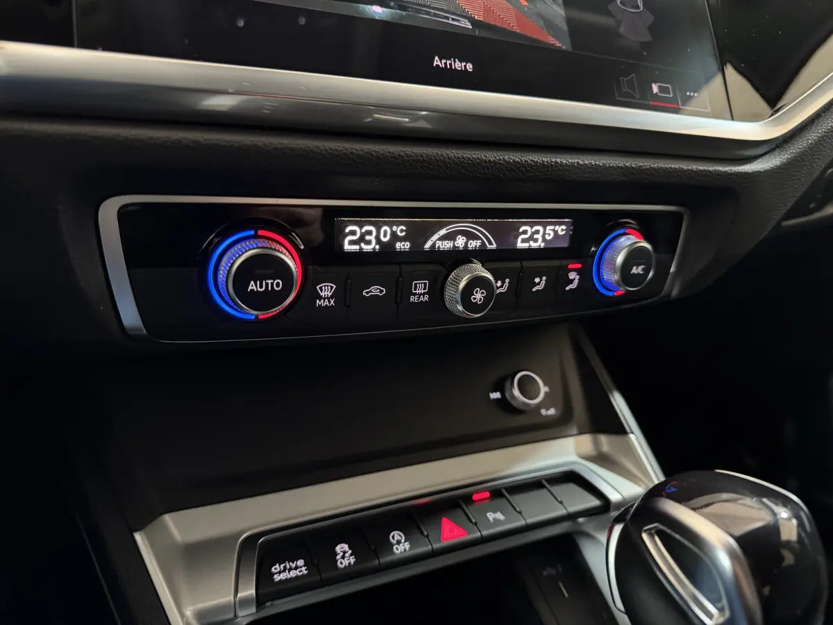 Gros plan sur la console centrale de l'Audi Q3 noire, montrant les commandes de climatisation digitale et la boîte automatique.