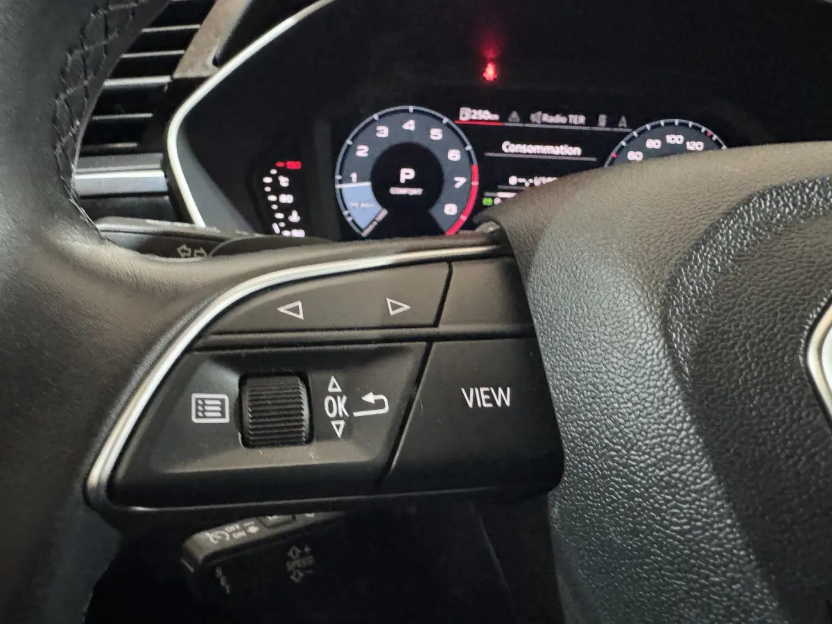 Gros plan sur le volant cuir noir d’un Audi Q3 2022, avec commandes multifonctions et tableau de bord numérique en arrière-plan.