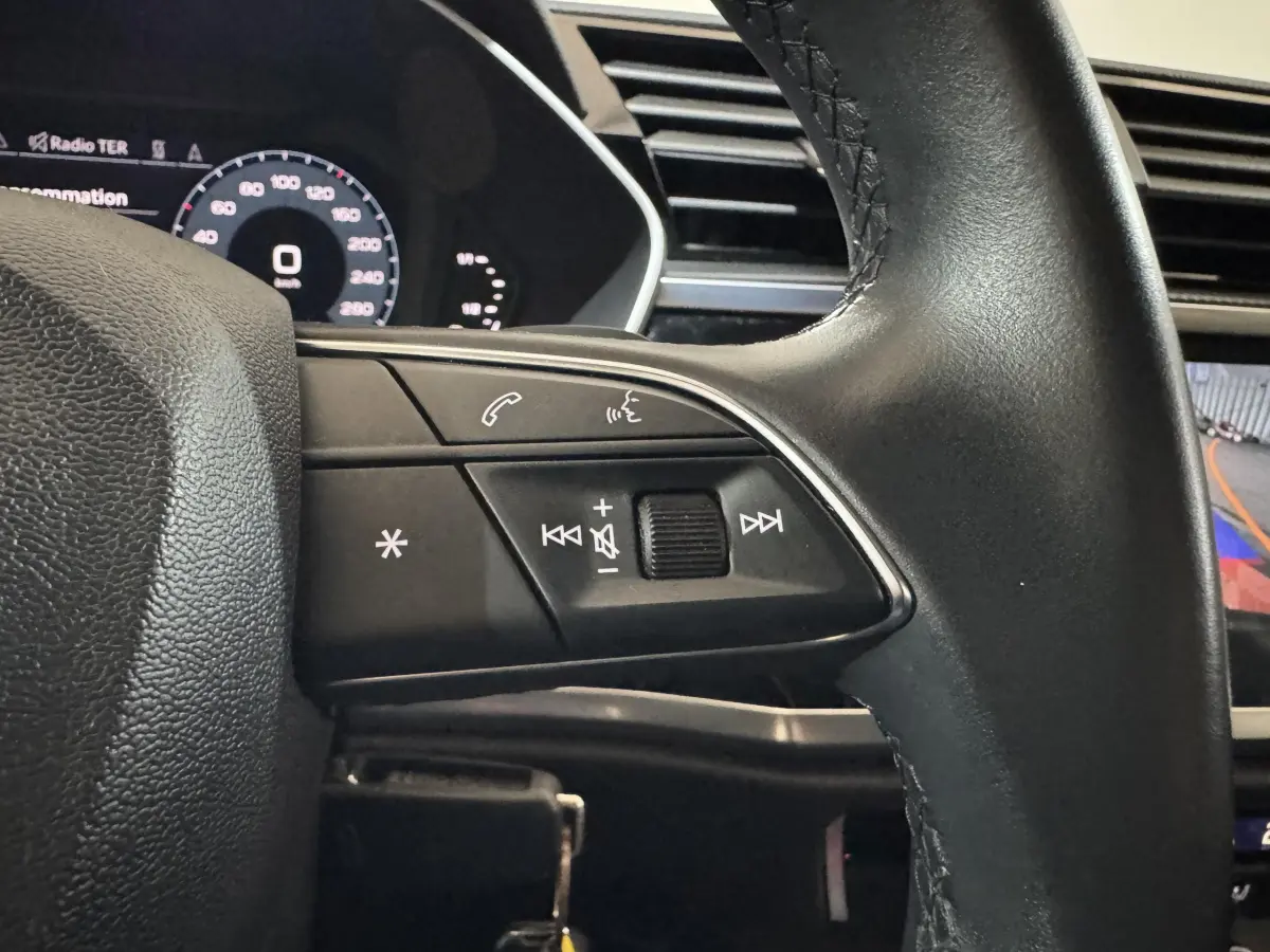 Gros plan sur les commandes au volant côté gauche d’un Audi Q3 noir, avec affichage digital et caméra de recul visible.