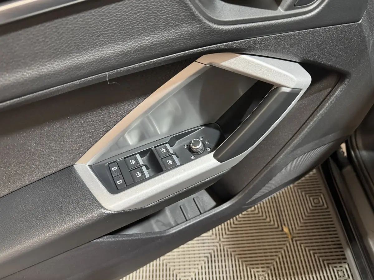 Détail des commandes de lève-vitres et rétroviseurs côté conducteur dans l'habitacle noir de l'Audi Q3 2022.