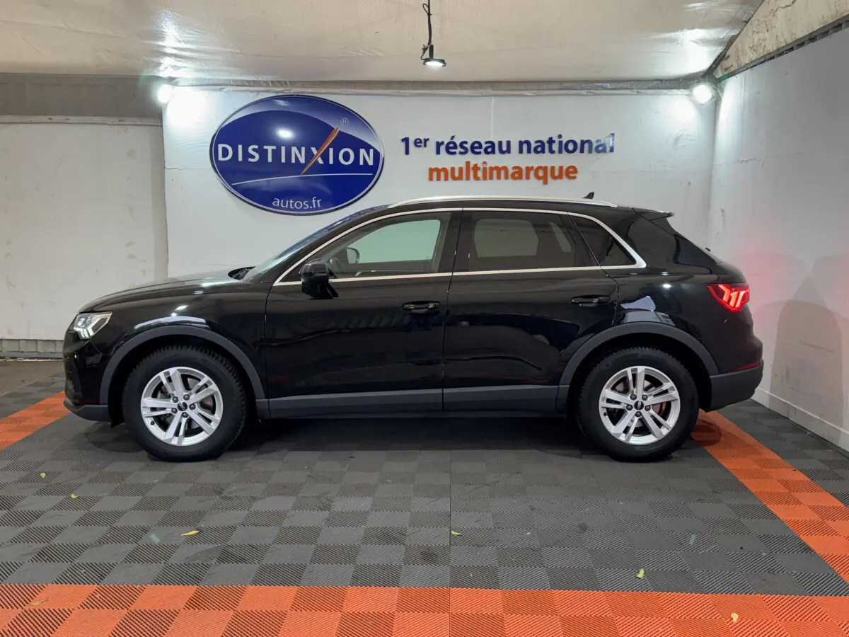 Audi Q3 noir vue de profil côté gauche dans un showroom avec éclairage et logo Distinxion en arrière-plan.