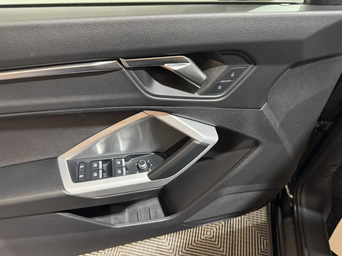 Gros plan sur la porte avant gauche noire de l'Audi Q3 35 TFSI avec commandes de vitres et serrure intégrées.